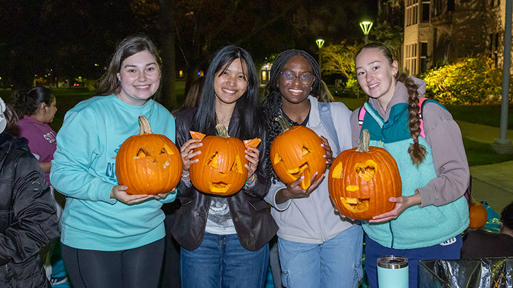 From left, Ella Smith, a freshman studying recreational therapy, Mary Polloso, a freshman studying health sciences; Vanessa Onyekelu, a freshman studying biology; and Olivia Kleshinski, a freshman studying communication, show off their pumpkin-carving skills at Monday night’s Carve-In & Chill in the front lawn of University Hall.