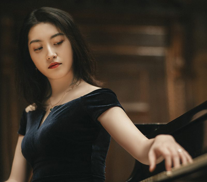 Portrait of Dr. Keer Wang sitting at a piano. She has performed for audiences across Asia, Europe and North America.