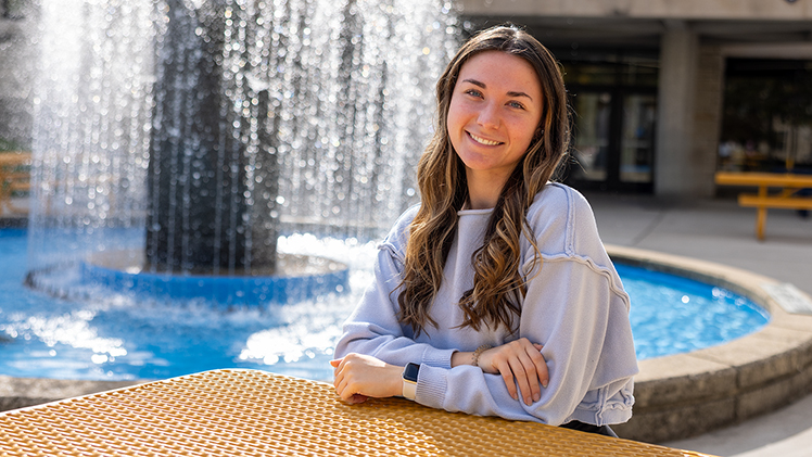 Outside photo of sophomore nursing student sophomore Mackenzie Bornhorst. Centennial Mall fountain is behind her.