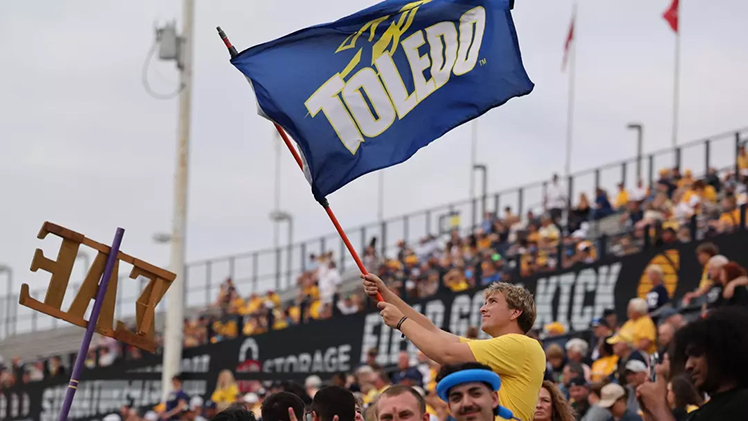 Crowd shot of a UToledo student waving the Toledo Rockets flag during a home football game.