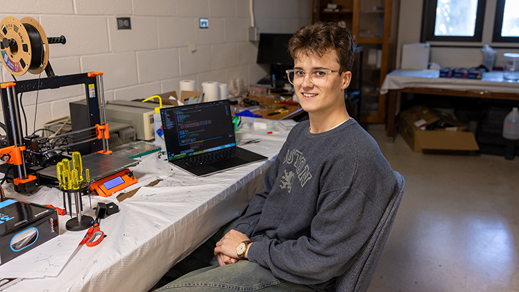 Portrait of junior William Gorgas in a research lab next to a laptop.