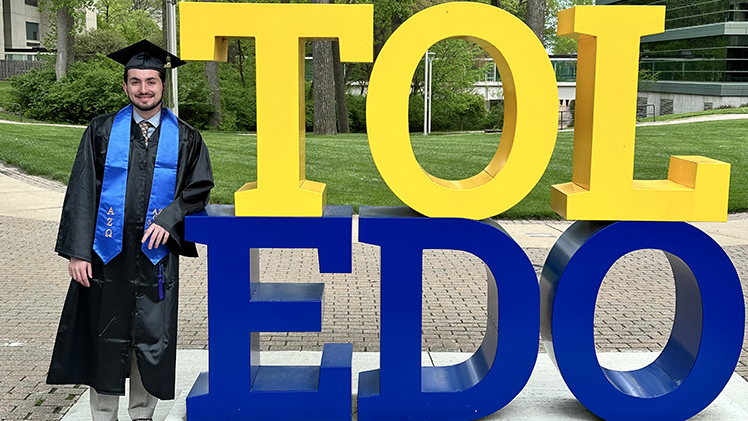 Photo of Pharm.D. student Zachary York in cap and gown posing net to the TOL-EDO sign.