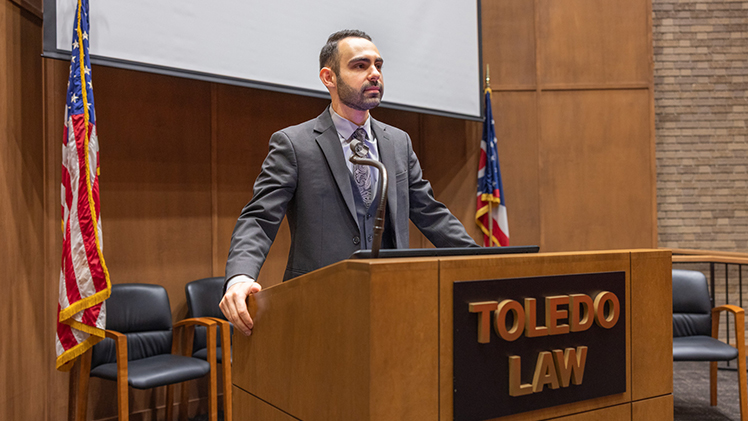 Portrait of UToledo law student Christian Karim, who is standing behind a Toledo Law podium.