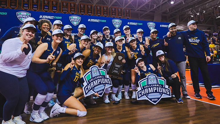 Photo of the UToledo Volleyball team and coaches posing for a group photo after winning the MAC championship for the first time in program history.