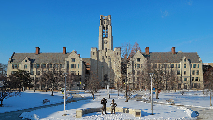 A photo of a snowy UToledo Main Campus with the mascot statues in the foreground and University Hall in the background. The sky is clear blue and there is no one on campus.