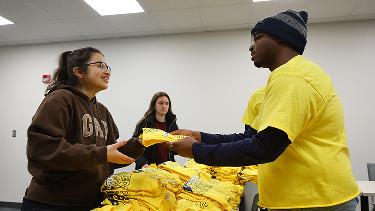 Undergraduate Assistant Joshua Ford hands a free shirt to Lisa Moguel (Senior majoring in Speech Language Pathology).