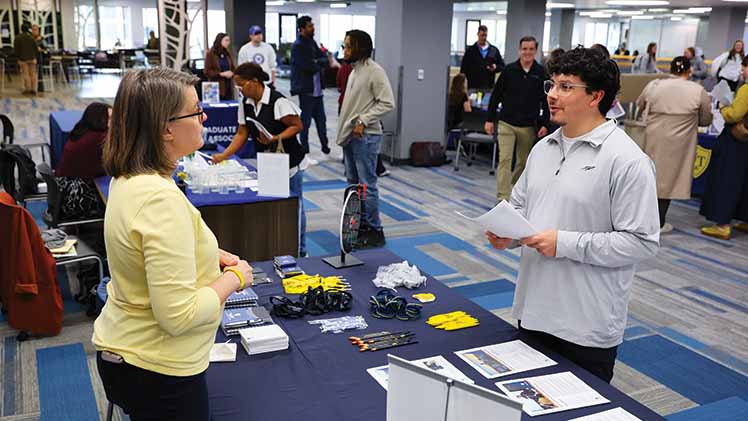 A UToledo staff member and student talk about a table at a UToledo Graduate Fair.