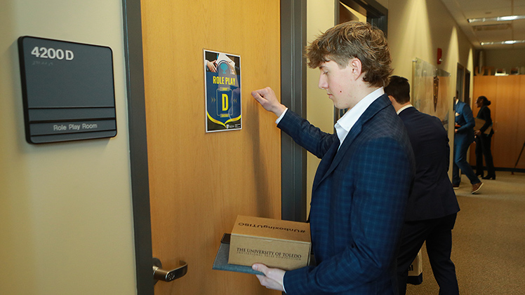 A student knocks on a door as part of a student team challenge to “sell” a product in role-play scenarios with corporate and faculty judges during the UToledo Invitational Sales Competition.