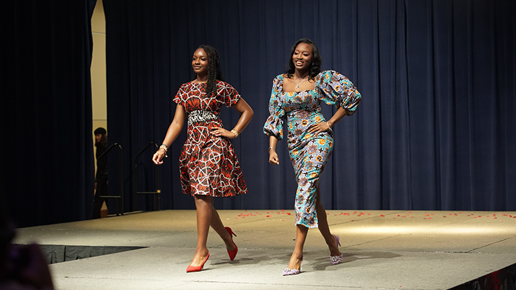 2 female students model fashionable dresses on the runway during the 56th annual Fashion Show on Tuesday night in Thompson Student Union Auditorium.