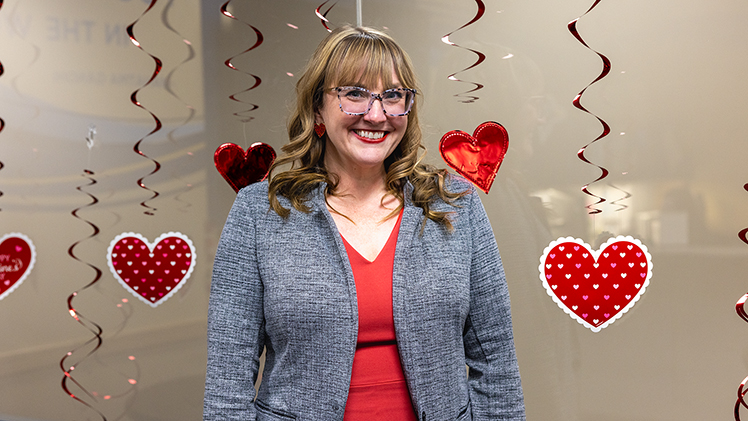 Portrait of Dr. Tasha Dunn an associate professor in the Department of Communication and Media at UToledo, who is standing in front of party decoration hearts hanging from the ceiling.