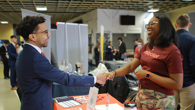 Undergraduate Jason Klotz shakes hands with Cassandra Wilson of Rocket Companies during the Spring 2025 Job Fair in Savage Arena.