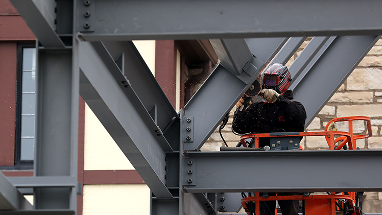 Construction worker sands steel framing on the new welcome center and one-stop center.