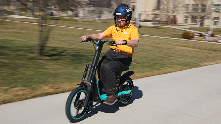 UToledo President James Holloway wears a UToledo football helmet as he rides a Veo electric bike on Main Campus.