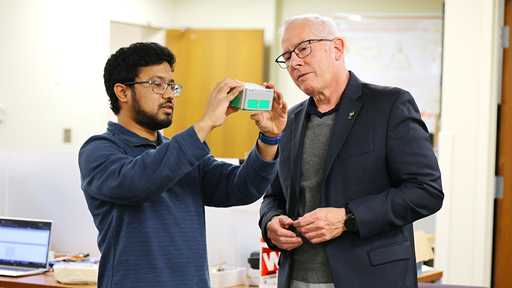 Md Faisal Karim, a master's degree student in electrical engineering, shows a prototype of the small satellite launching on Sunday to UToledo President James Holloway.