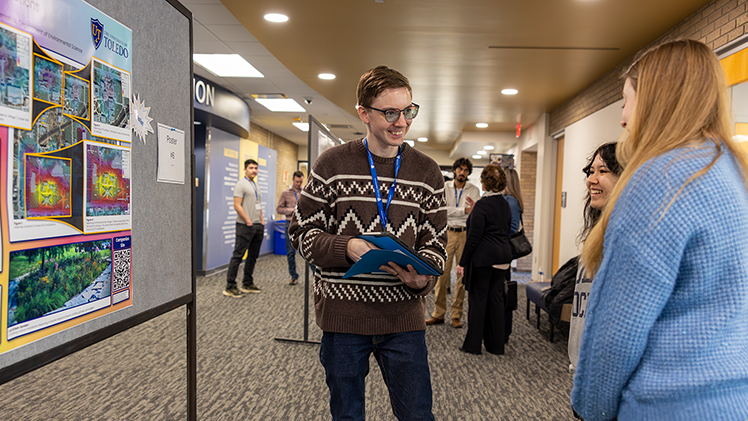 Justin Myers, left, a senior studying environmental sciences, explains his research poster, "Growing with Purpose: A GIS model for Future GUTS installations," to Keyleen Cleavenger, center, a junior in digital communication, and Emma Moon, right, a junior in media communication, during the Office of Undergraduate Research’s Undergraduate Research and Creative Activity Exhibition on Friday at Carlson Library.
