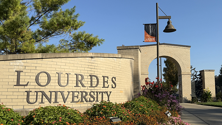 ALT: Photo of the Lourdes University outdoor sign with flowers in front of it.