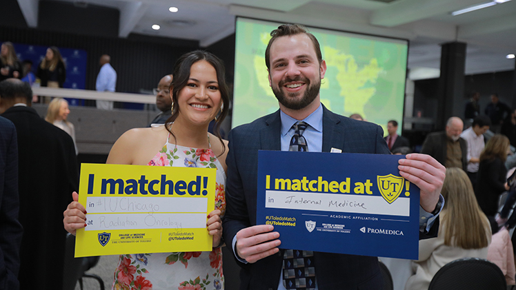 2 fourth-year med students hold their "I Matched" signs during the College of Medicine and Life Sciences Match Day.