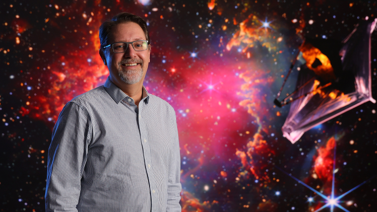 Dr. Michael Cushing stands in front of a space photo backdrop.