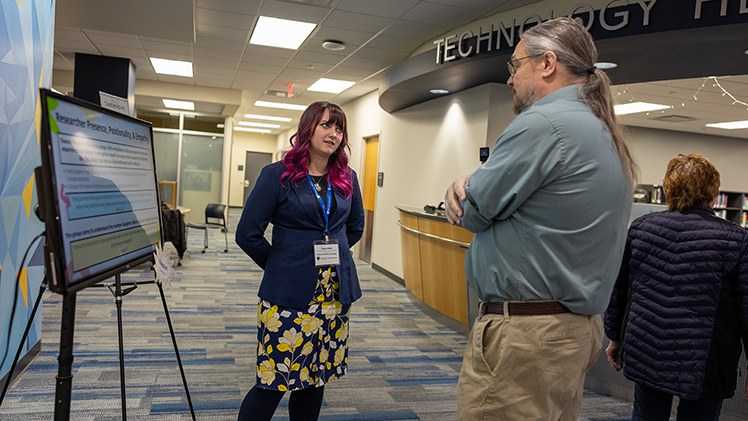 Taylor Kiffel, a junior communication student, talks with Professor Wade Lee-Smith, a research engagement librarian and science reference librarian, about her research on mother-daughter relationships in media at the Office of Undergraduate Research’s Undergraduate Research and Creative Activity Exhibition at Carlson Library. 