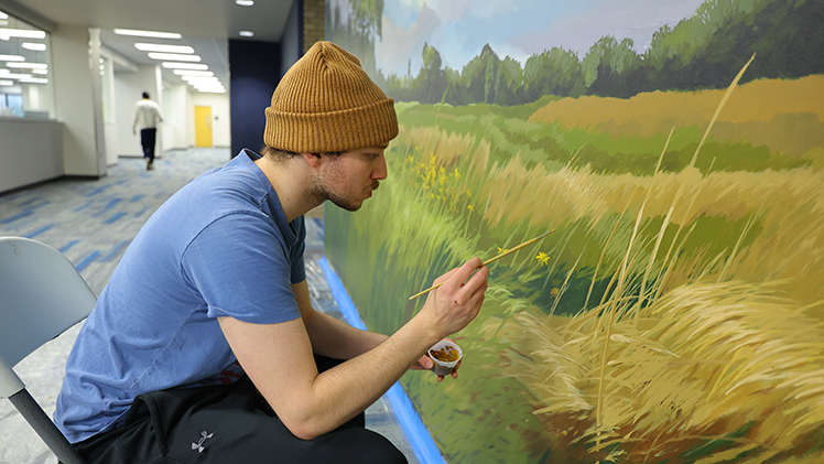 Toledo-based artist and 2025 UToledo alumnus Liam Ginter works on a new native plant mural inside Carlson Library. The collaborative experiential learning project, which bridges art, science and sustainability, depicts Lucas County's rare oak prairie biome and native flowering plants.