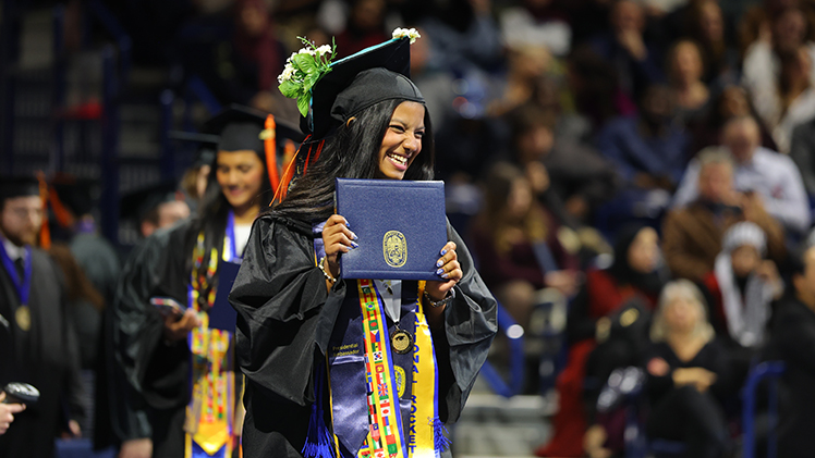 A female student smiles for a photo after walking across the UToledo commencement stage. 