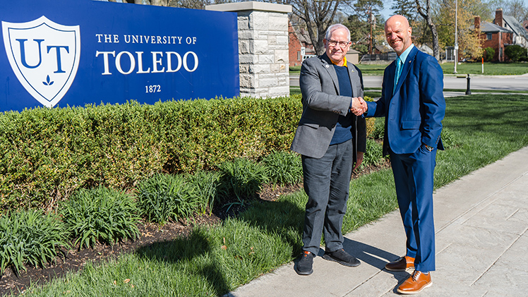 UToledo President James Holloway and Junior Achievement of Northwestern Ohio President Jim Pollock shake hands in front of a UToledo sign.