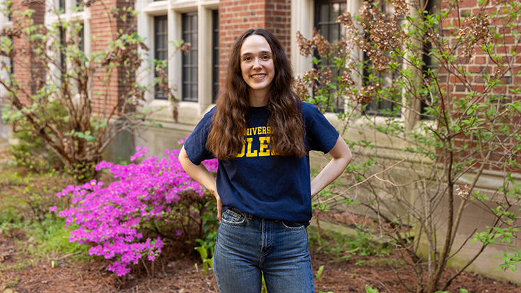 Graduating senior Sophia Durham poses outside with a flowering bush behind her.
