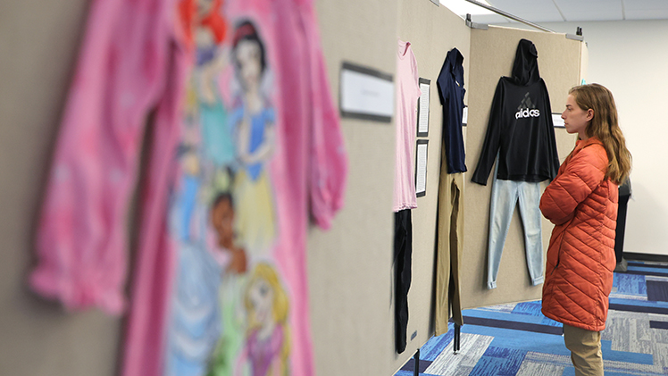 Sarah Jolliff, an M.B.A. student in information systems and an institutional compliance specialist, reads a testimonial at the “What Were You Wearing?” installation on display from 10 a.m. to 4 p.m. through Thursday, April 9, in Carlson Library Room 1005.