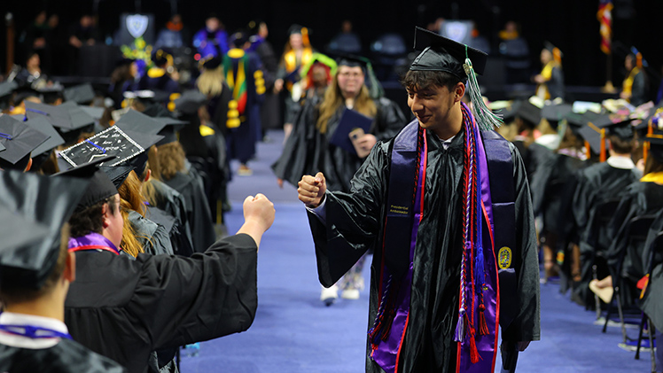 Alex Hudson, standing, offers a celebratory fist bump to his friend A.J. Grabarczyk during the afternoon ceremony. Hudson graduated with a bachelor’s degree in exercise science and Grabarczyk graduated with a bachelor’s degree in professional sales.