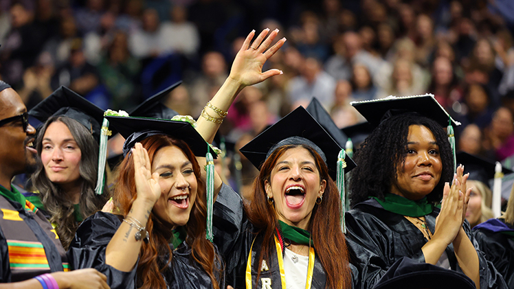Elicia Garces, left, Emily Montaser-Salhi and Olivia Johnson cheer and wave to the crowd during Saturday's commencement ceremony inside Savage Arena. All three graduated with master of social work degrees.