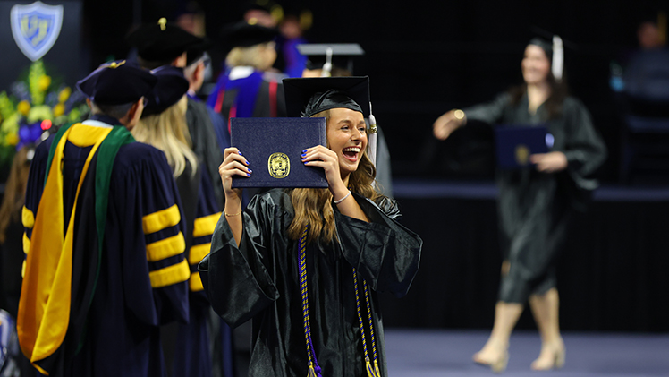 Brooke Wise smiles as she holds up her diploma cover after crossing the stage during Saturday's commencement ceremony inside Savage Arena. Wise graduated with a bachelor's degree in communication.