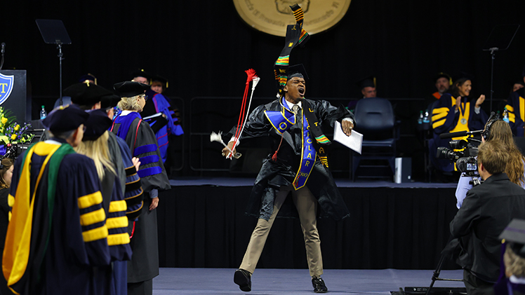 Derell Bedingfield Jr. leaps into the air in celebration while crossing the stage during Saturday's commencement ceremony inside Savage Arena. Bedingfield graduated with a bachelor's degree in communication.
