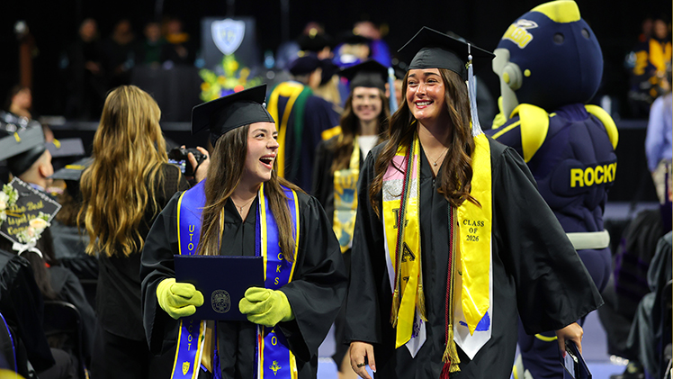 Jill Kromer, left, and McKenna Nunez share a laugh during Saturday's commencement ceremony inside Savage Arena. Both graduated with degrees in early childhood education. Kromer is wearing the signature yellow gloves of UToledo mascot Rocksy.