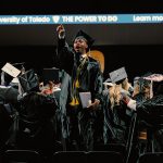 During a spring 2026 commencement ceremony, a UToledo student who has just graduated points to the stands in celebration.