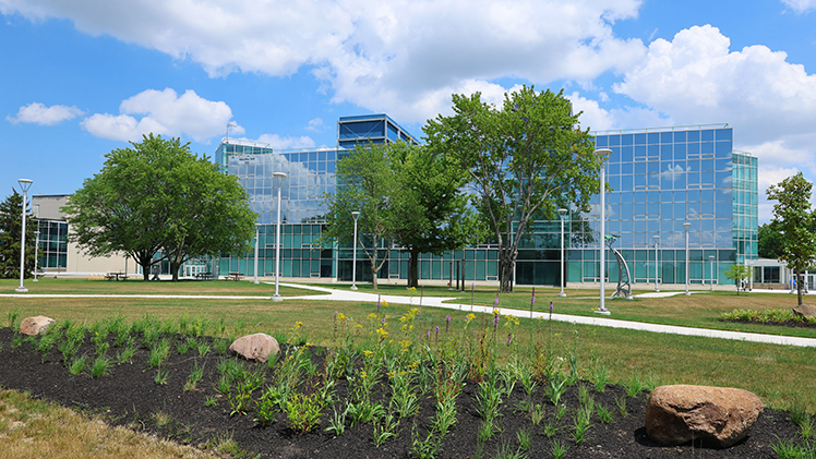 Stock photo of the UToledo Engineering building on a sunny day with flowers in front of it.