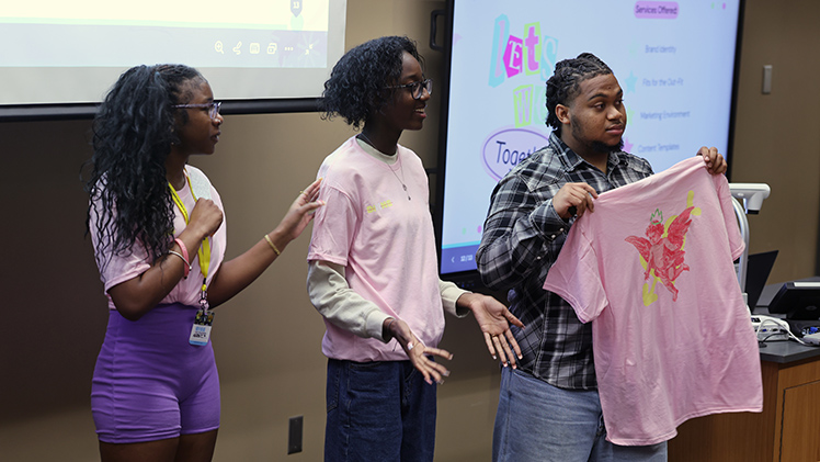 From left, high school students Shia Carey (Toledo School for the Arts), Jayla Gover (St. Ursula) and Solomon Alexander (Jones Leadership Academy of Business) present their business plans for selling T-shirts to a “Shark Tank”-style panel Wednesday afternoon at The RISE Into Business summer enrichment camp.