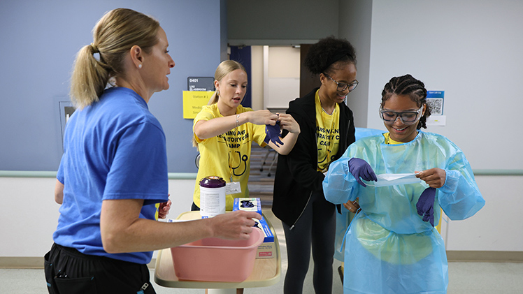 From left, registered nurse Ecole Charley, and campers Bridget Brooks, Castle Quinn and Aliyah Franklin compete in a surgical personal protective equipment (PPE) relay at the Nursing and Respiratory Care Camp hosted by the College of Health and Human Services.