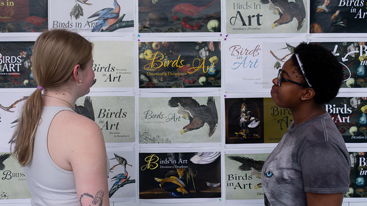 2 female UToledo art students look at postcards for an online exhibit they helped curate for the Toledo Museum of Art.