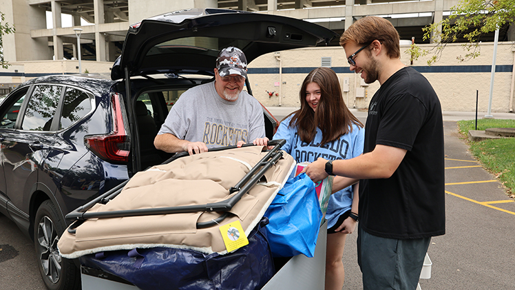 A Rocket Welcome Crew volunteer helps a student and family member unload belongings during residence hall move-in.