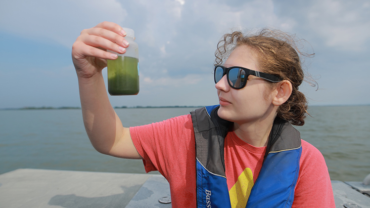 Female student conducts algae testing on a UToledo research boat.