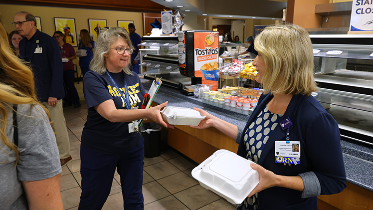 Danielle Kasack, assistant nurse director of outcome management, hands a lunch box to Lisa Keaton, a transplant social worker, during Employee Appreciation Summerfest 2026.