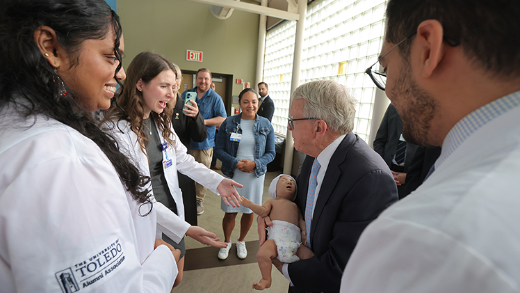 UToledo MD student Mary Grace Hamlin holds out her arms to take an infant patient simulator from Gov. Mike DeWine.