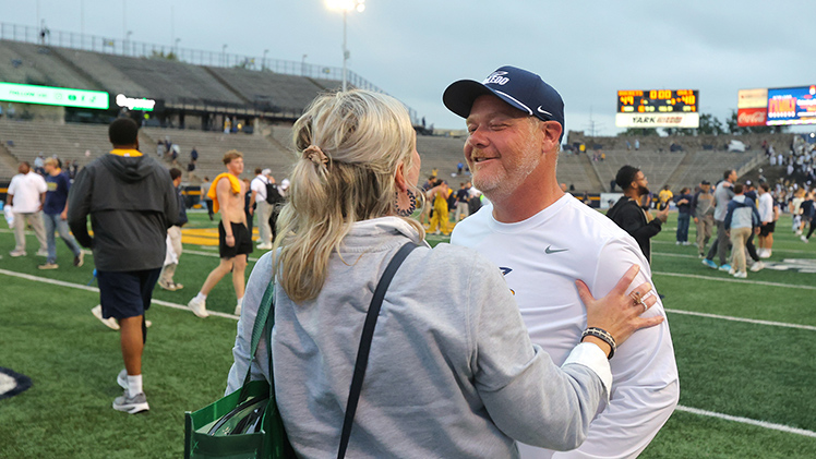 First-year Head Coach Mike Jacobs meets with his wife, Lacey Jacobs, on the field following his team's big win at Glass Bowl Stadium.