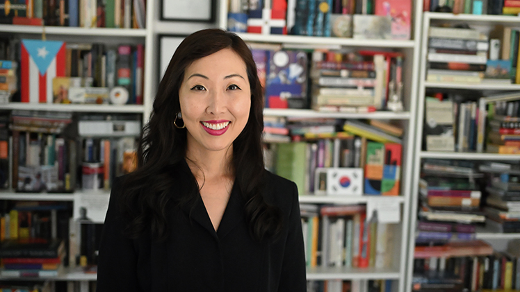 Portrait of UToledo Associate Professor of English Joey Kim, with a bookshelf full of books behind her.