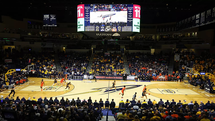Wide photo of men's basketball game with full court and fans.
